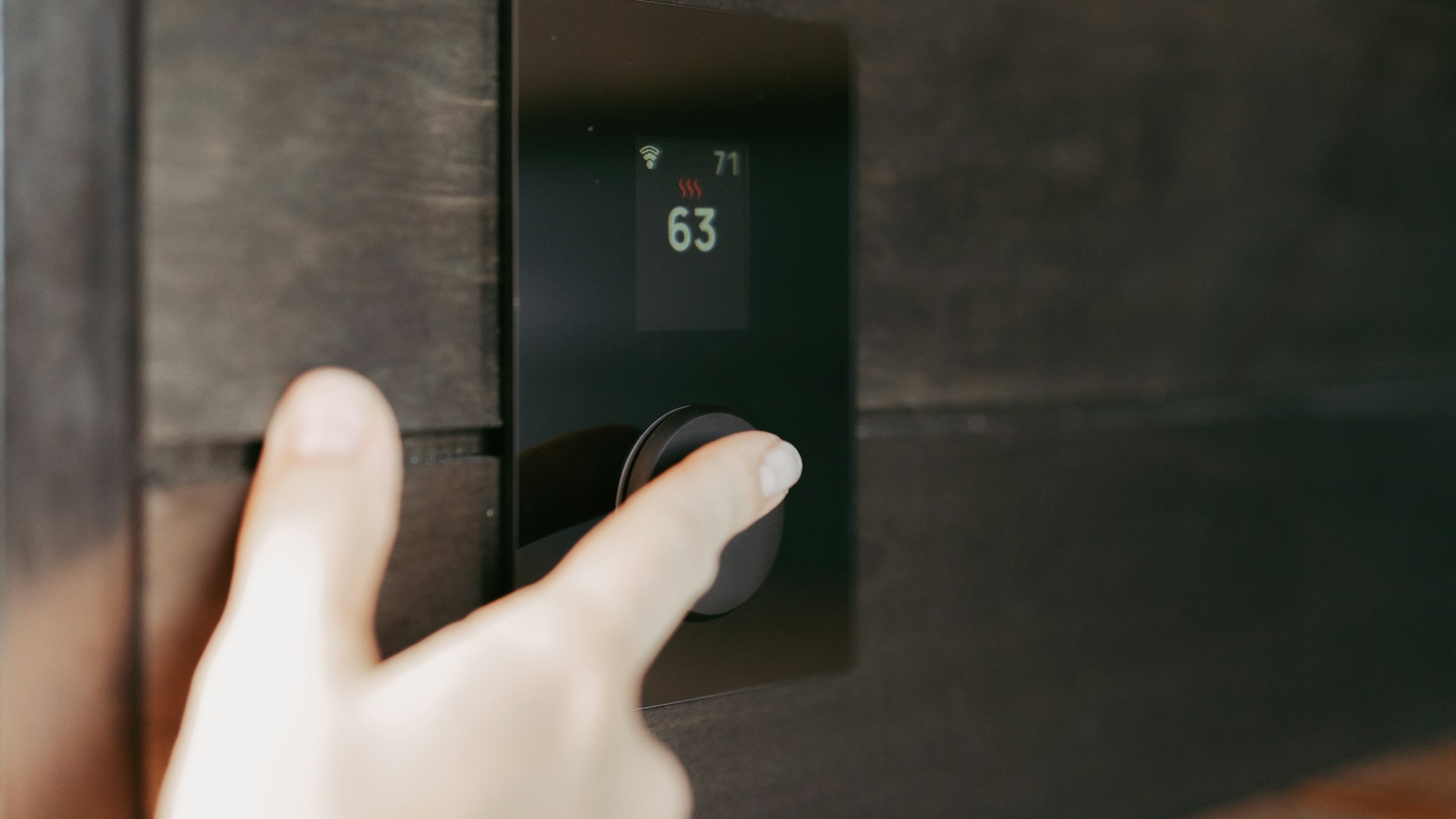 Hand an einem digitalen Bedienpanel für die Raumtemperatur